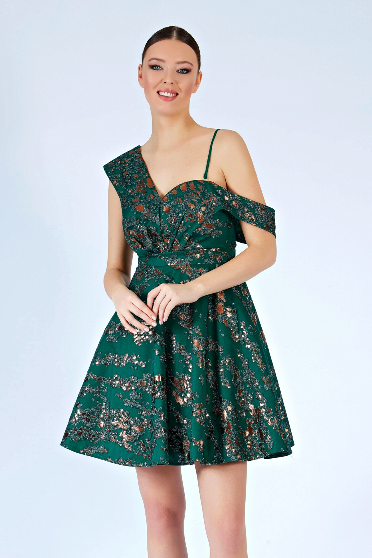 Abito corto svasato verde smeraldo con fantasia glitterata e spalla cadente, marca Moda-Mania, in tessuto elegante e sofisticato.
