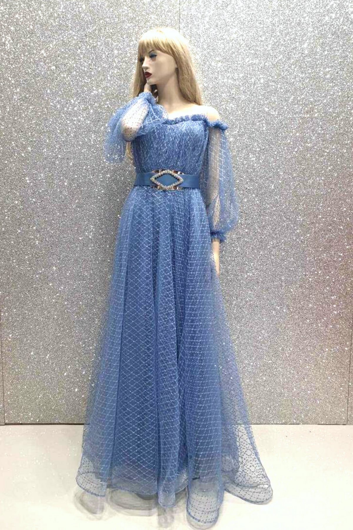 Abito lungo elegante celeste Moda Mania in tulle fantasia con scollo a barchetta e maniche lunghe, visibile nella foto.