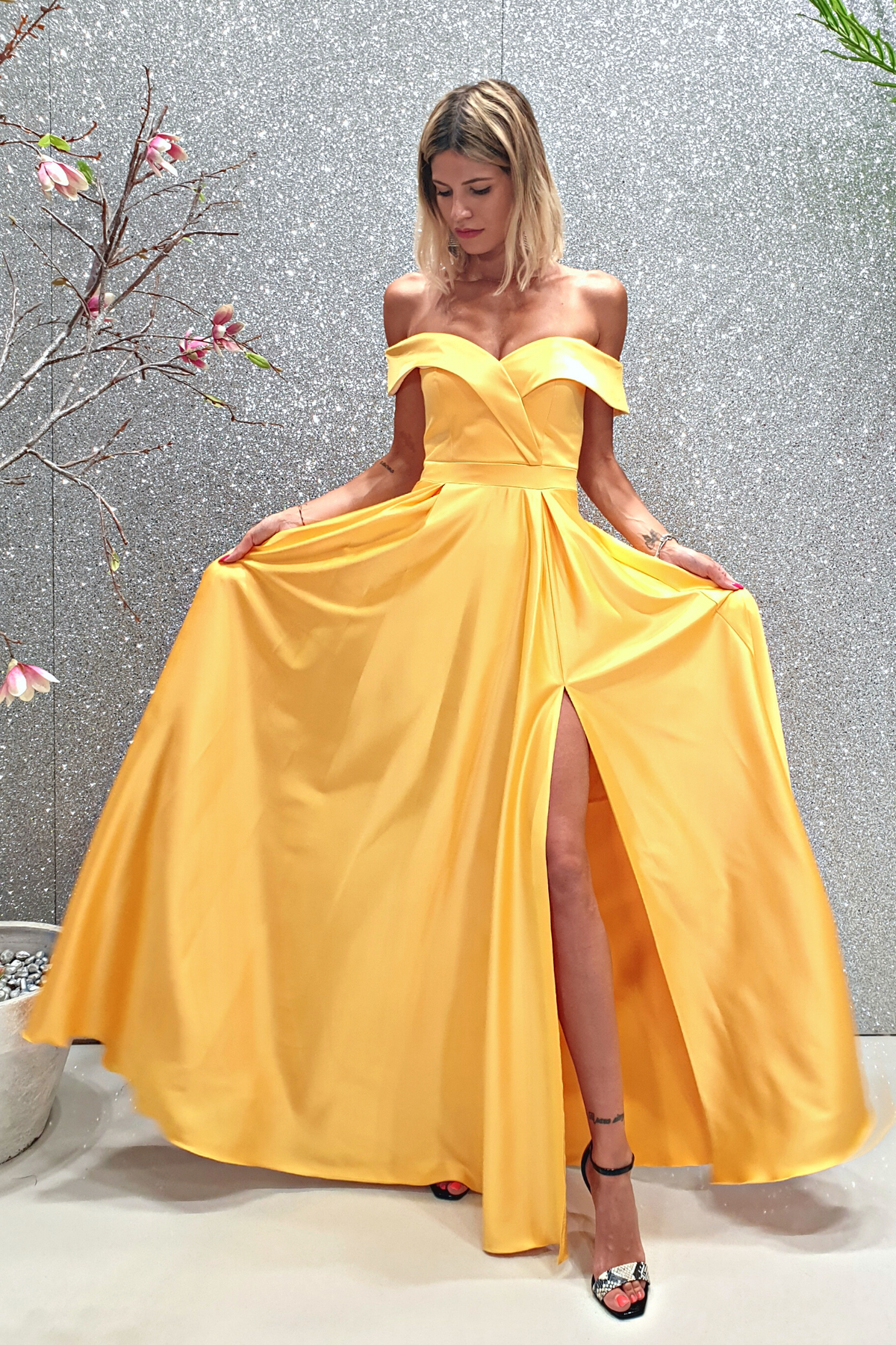 Abito lungo svasato giallo in taffetà con scollo a barchetta e spacco laterale, firma Moda-Mania, in tessuto lucido e elegante.
