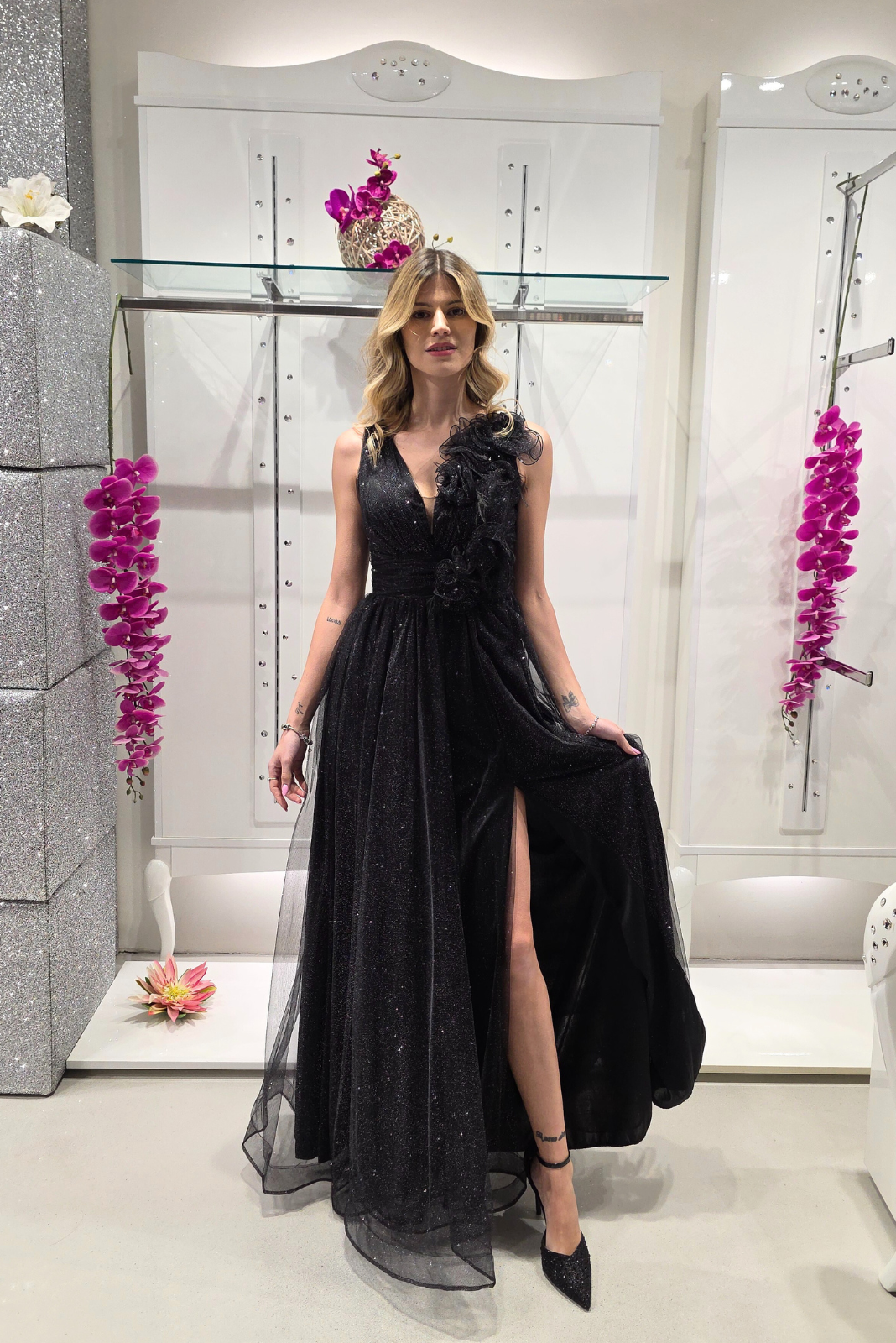 Abito lungo svasato nero in tulle glitterato con spacco e dettagli floreali, firmato Moda-Mania, indossato in primo piano.