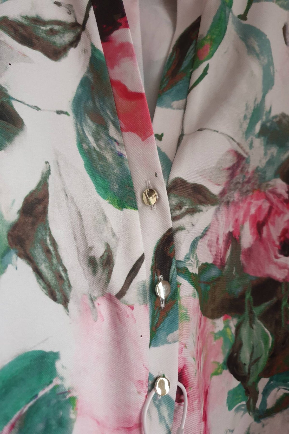 Blusa bianca Moda-Mania con fantasia floreale rosa e foglie, maniche tre quarti e bottoni dorati, dettagli eleganti.