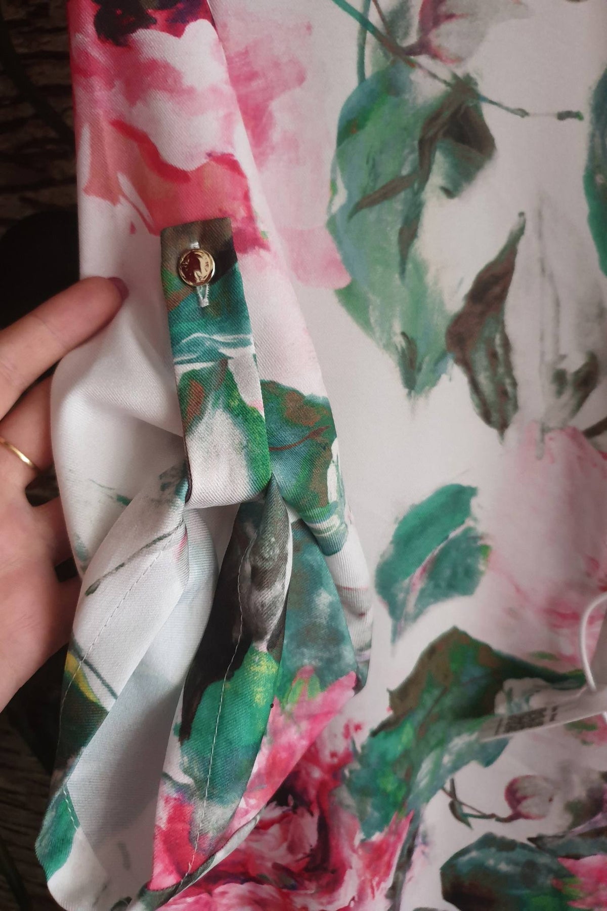 Blusa bianca Moda-Mania con fantasia floreale rosa e foglie, maniche tre quarti e bottoni dorati, dettagli eleganti.