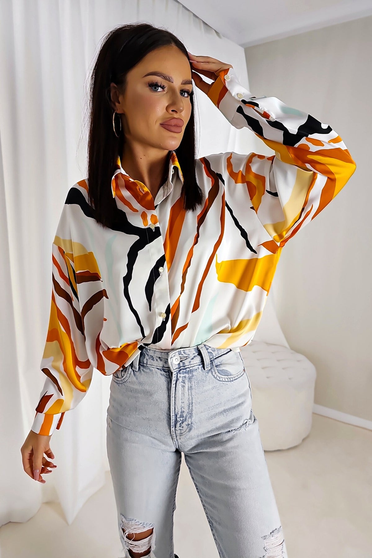 Camicia bianca larga Moda-Mania con fantasia astratta arancione, giallo e nero, tessuto satinato lucido con bottoni dorati.