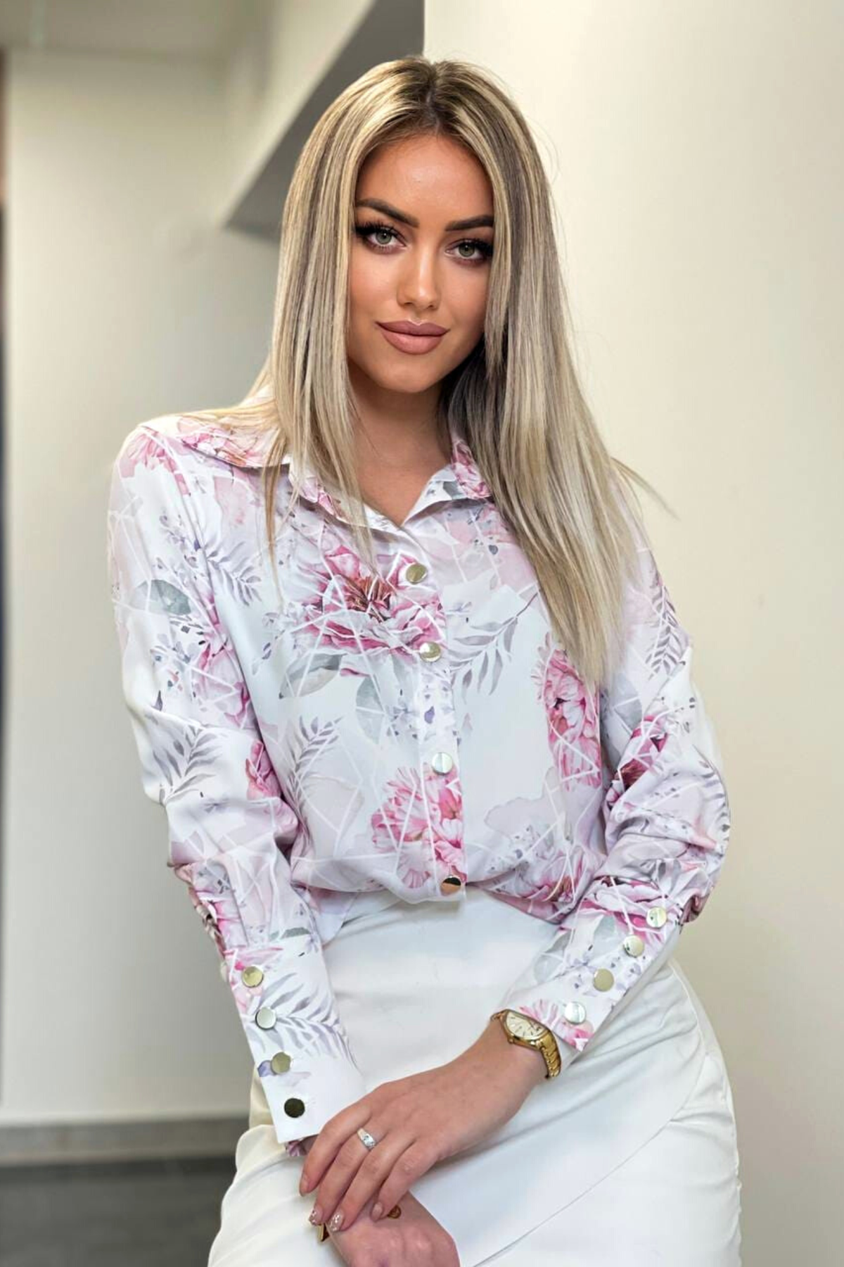 Camicia elegante bianca con fantasia floreale rosa, bottoni dorati, marca Moda-Mania, dettagli raffinati e tessuto leggero.