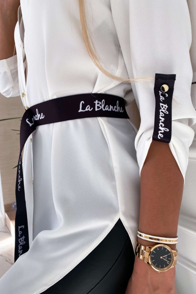 Camicia lunga bianca con taglio asimmetrico accessoriata con cintura nera