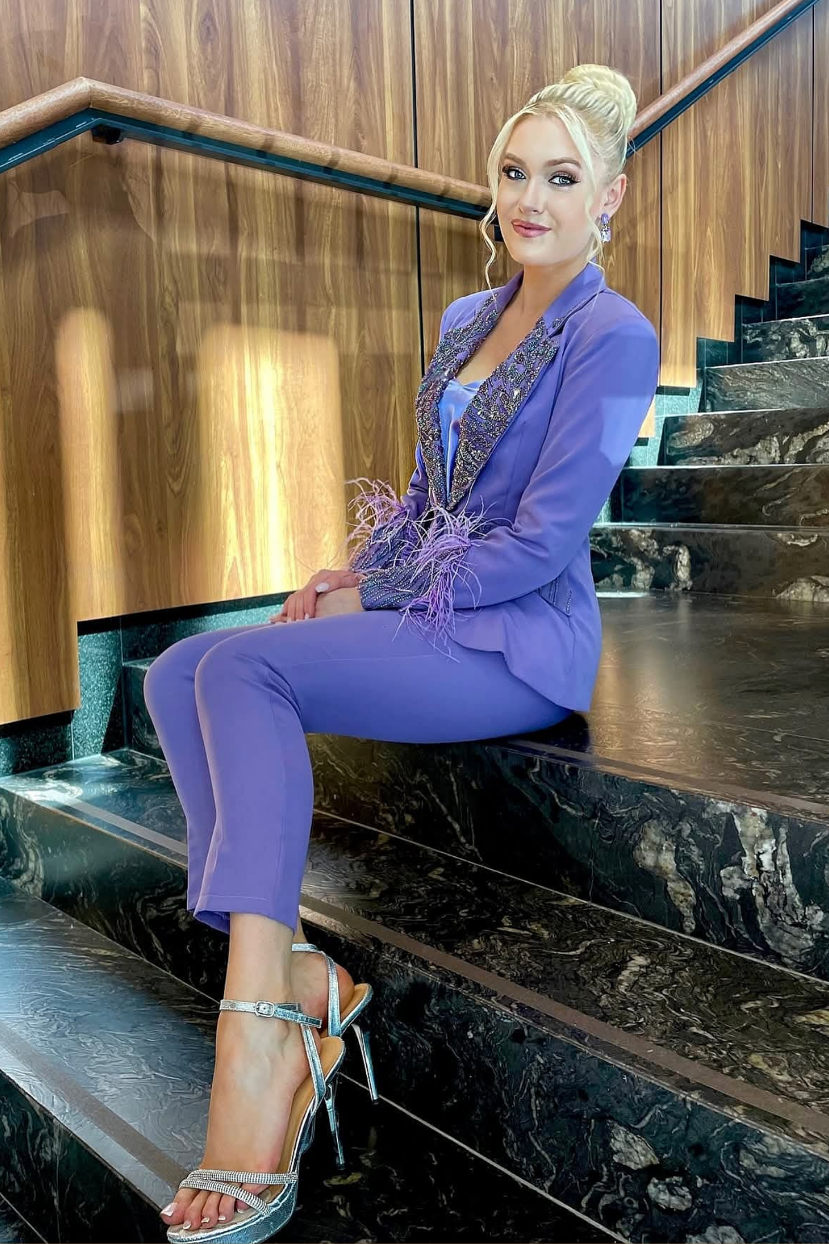 Completo tailleur Bby con giacca lilla impreziosita da piume e ricami in perline, con pantaloni a sigaretta eleganti.