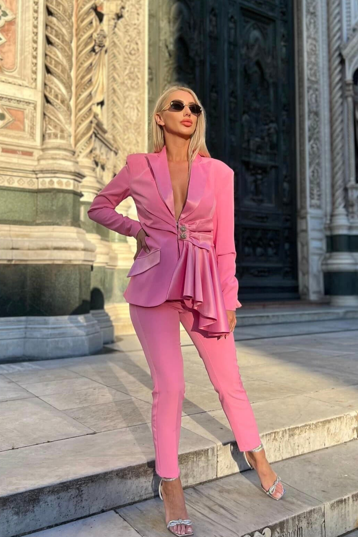Completo tailleur rosa Bby con giacca e pantalone, bottoni gioiello, volant, fiocco e dettaglio cut-out in vita.
