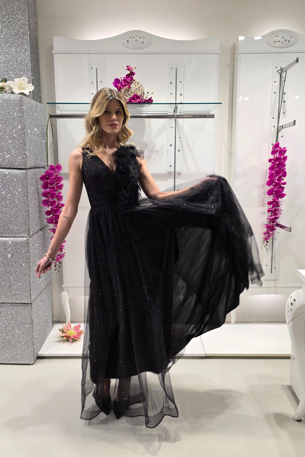 Abito lungo svasato nero in tulle glitterato con spacco e decorazioni floreali, design elegante di Moda-Mania.