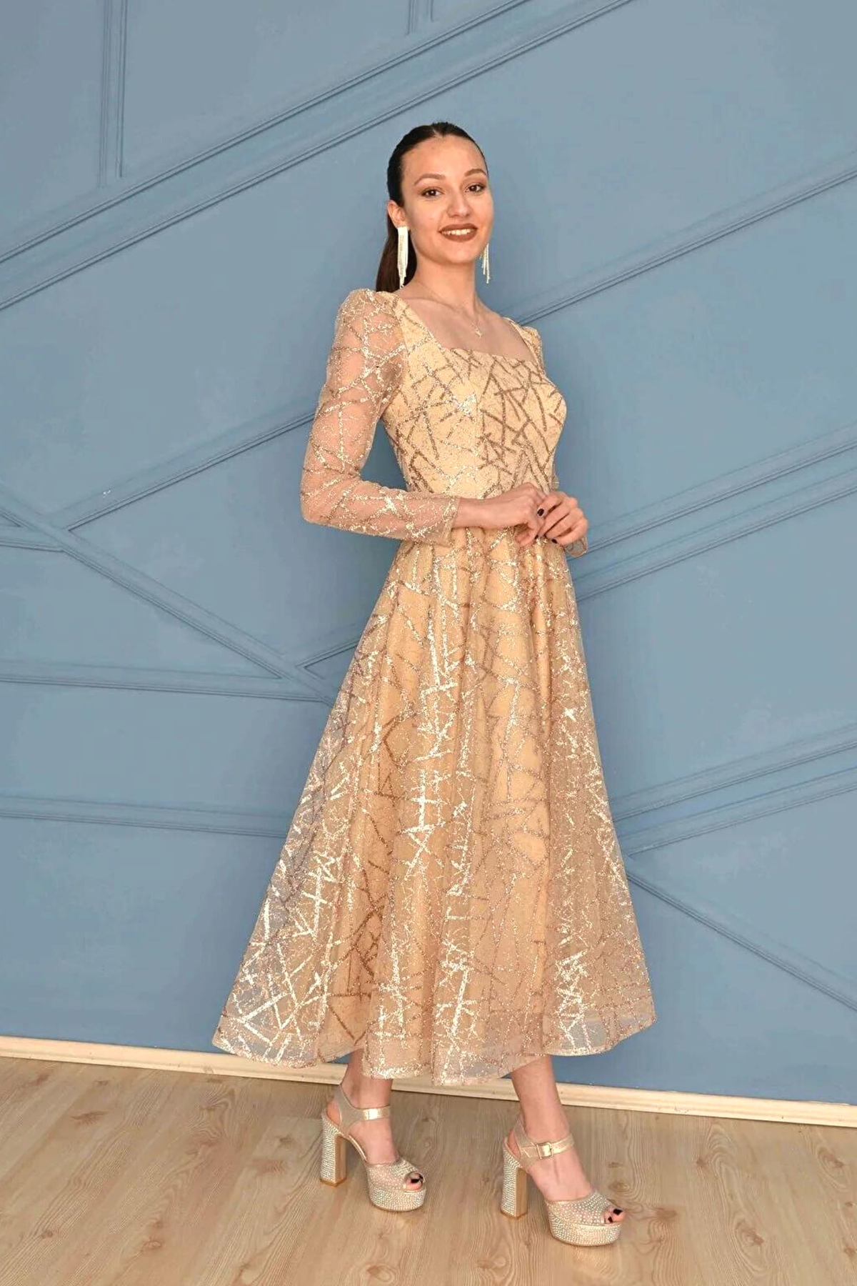 Abito svasato midi in tulle con trama glitterata dorata e maniche lunghe, firma Moda-Mania, su modello vestito elegante.