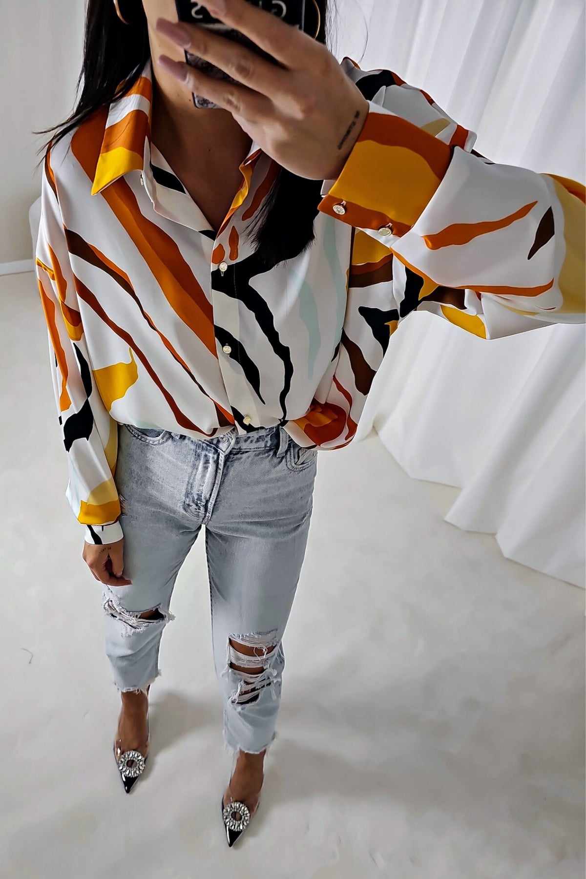Camicia bianca larga Moda-Mania con fantasia astratta arancione, giallo e nero in tessuto satinato lucido con bottoni dorati.