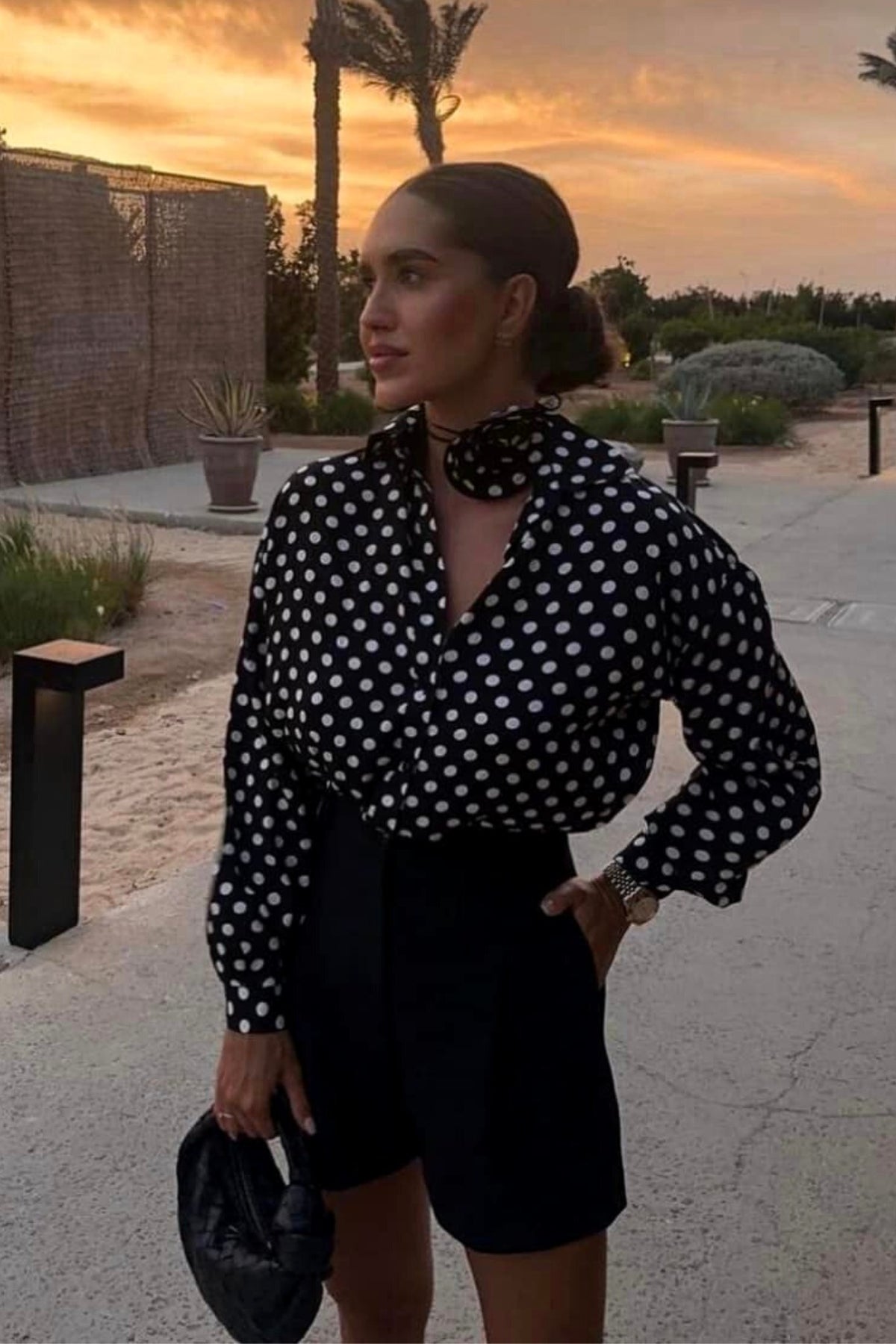 Camicia nera in viscosa con pois bianchi, accessoriata con fiore in tessuto, moda-mania, abbigliamento femminile elegante.