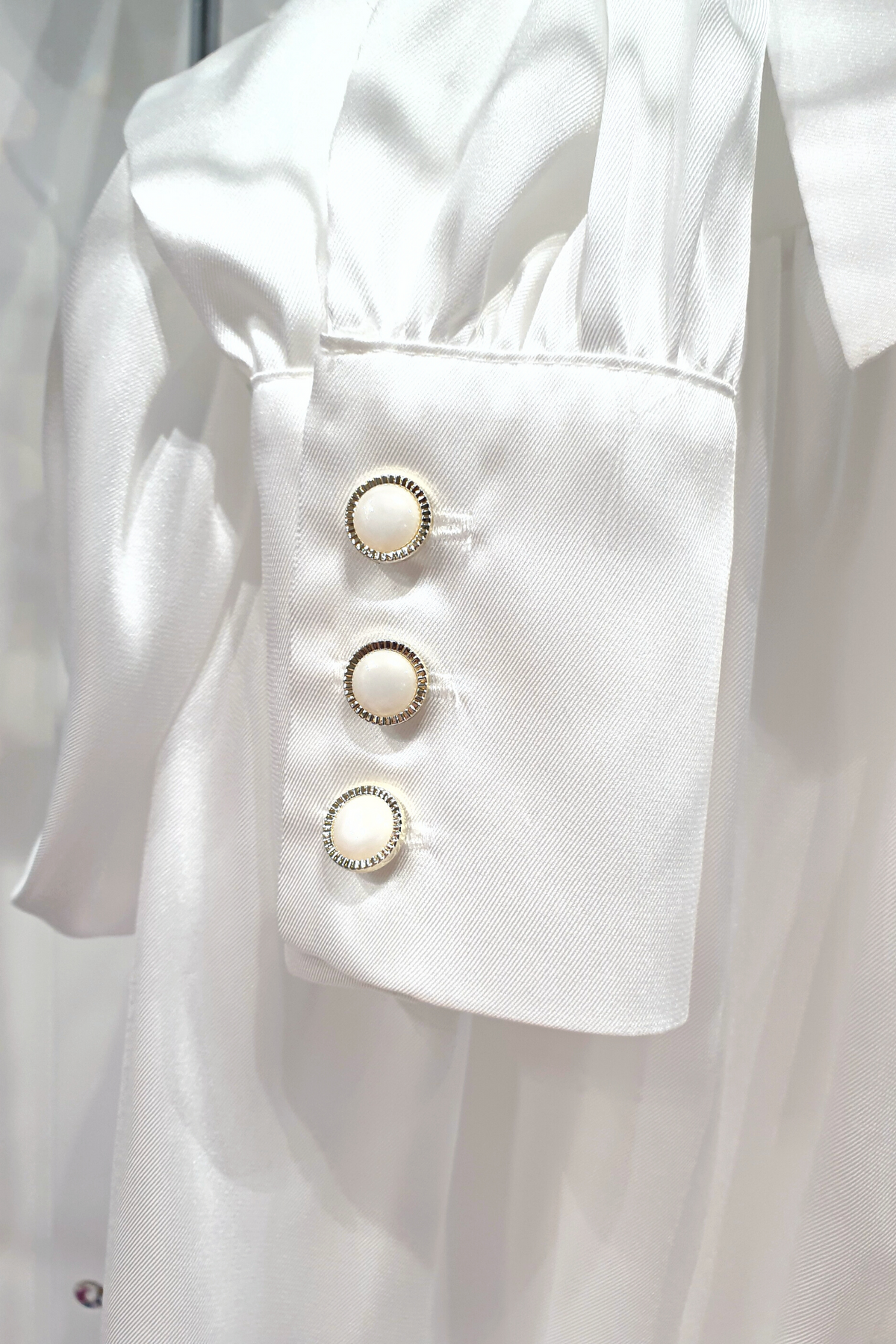 Camicia elegante bianca in tessuto satinato con maniche a sbuffo e bottoni gioiello, marca Moda-Mania, vista frontale.