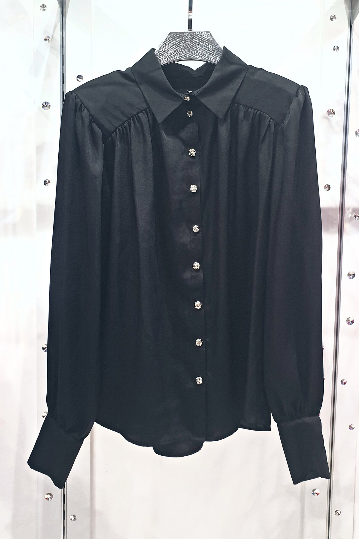 Camicia elegante nera Moda-Mania in satin con maniche a sbuffo e bottoni gioiello bianchi, tessuto lucido e raffinato.