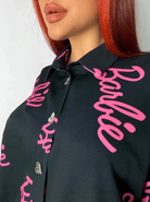 Camicia oversize nera Moda-Mania con scritta fucsia Barbie, bottoni a forma di cuore dorati, stile casual e trendy.