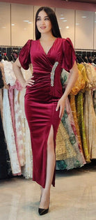 Abito lungo aderente bordeaux in velluto con scollo a V, spacco laterale e accessorio in cristalli, da Moda-Mania.