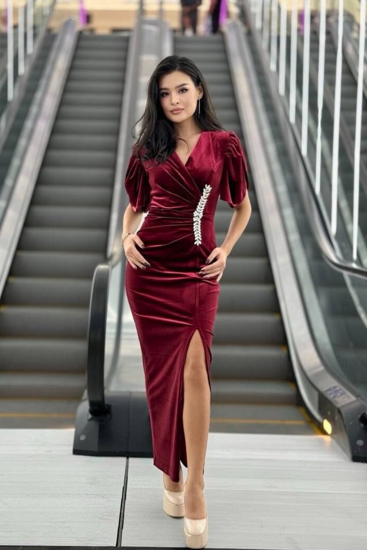 Abito lungo aderente bordeaux in velluto con scollo a V, spacco laterale e accessorio in cristalli, firmato Moda-Mania.