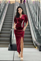 Abito lungo aderente bordeaux in velluto con scollo a V, spacco laterale e accessorio in cristalli, firmato Moda-Mania.