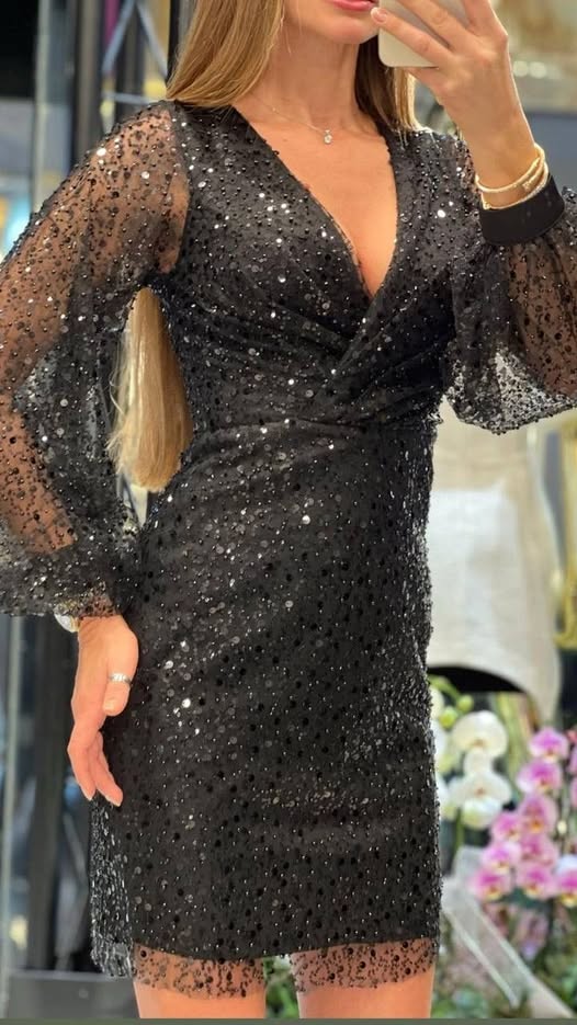 Abito corto nero aderente in tulle con paillettes e perline nere, scollo a V e maniche lunghe a sbuffo.