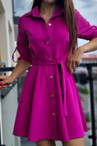 Abito camicia svasato colore magenta Moda-Mania con bottoni dorati e cinturino, vista frontale su tessuto leggero e dettagli eleganti