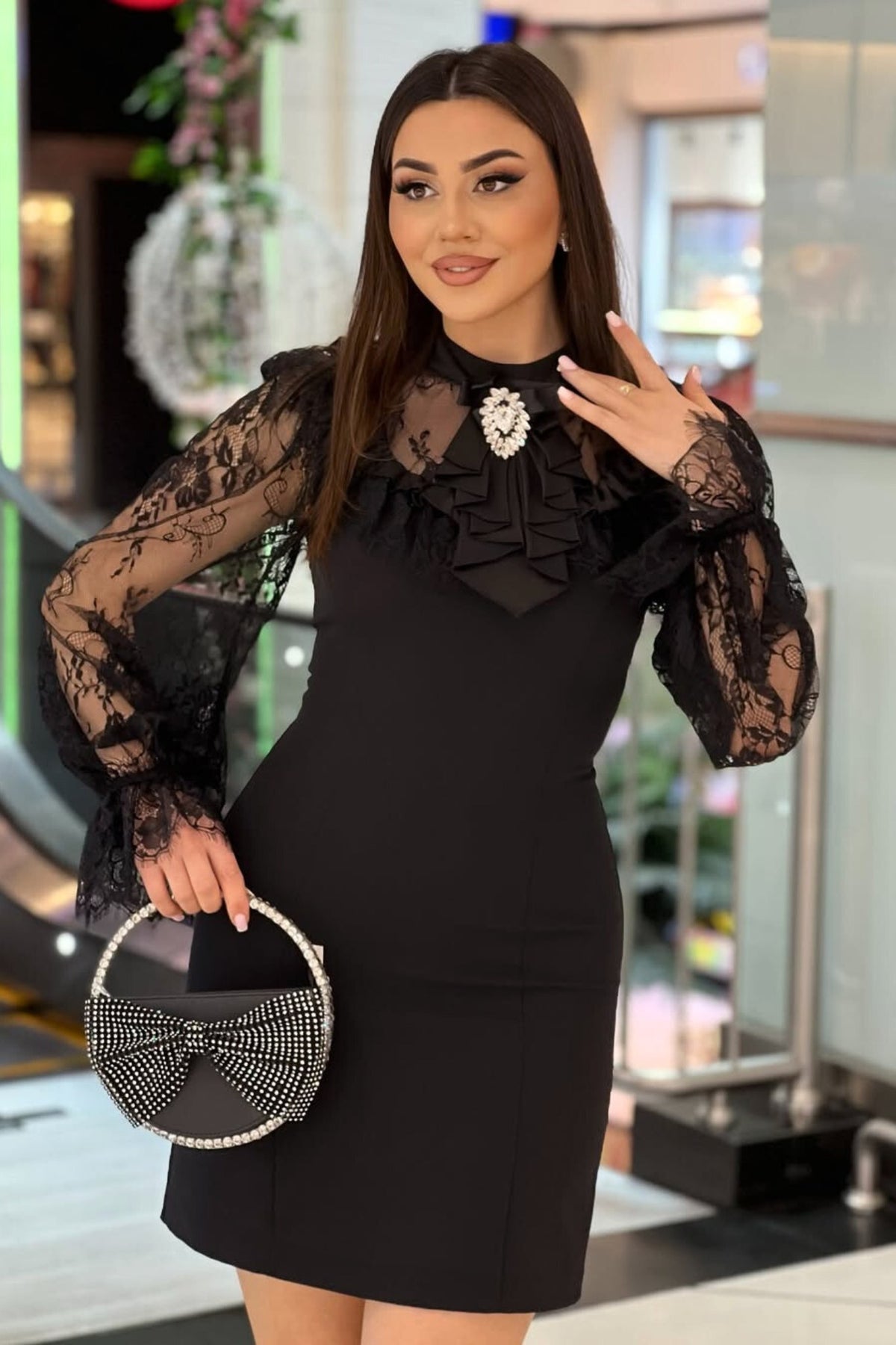 Abito corto nero linea dritta con maniche in pizzo e spilla decorativa moda-mania, elegante e femminile, dettaglio in pizzo e accessorio.