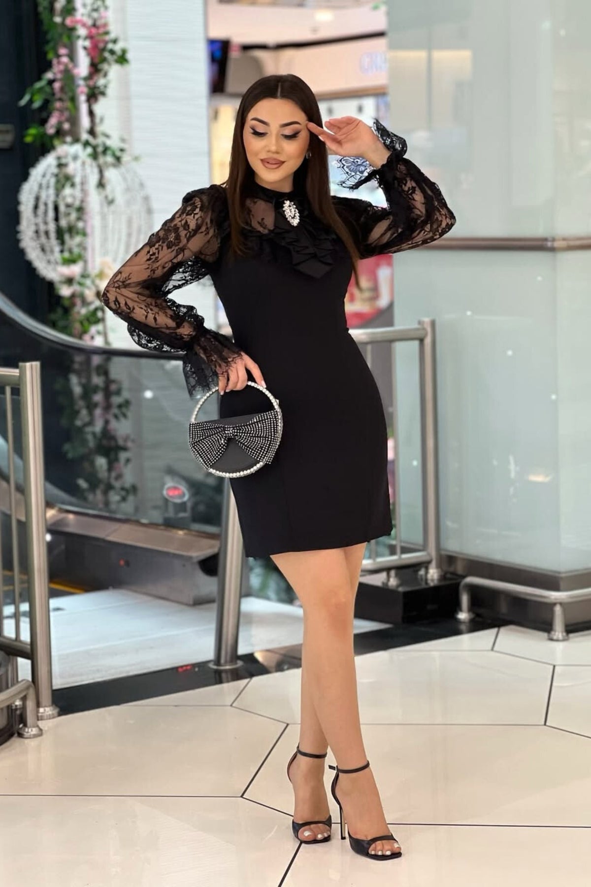 Abito corto nero linea dritta Moda-Mania con maniche in pizzo e spilla decorativa, vestibilità elegante e dettagli raffinati.