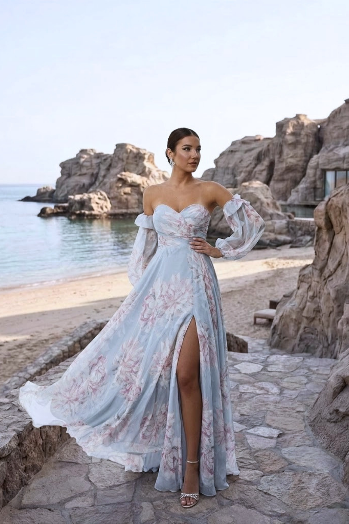 Abito lungo celeste con fantasia floreale in georgette, scollo a cuore e maniche lunghe rimovibili, firmato Moda-Mania.