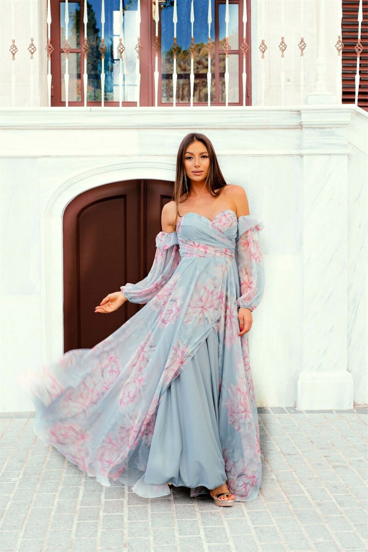 Abito lungo celeste con fantasia floreale in georgette, scollo a cuore e maniche lunghe rimovibili, firmato Moda-Mania.