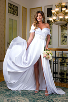 Abito lungo svasato bianco Pretty Girl con spacco laterale e fibbia gioiello, vestito elegante in tessuto leggero.