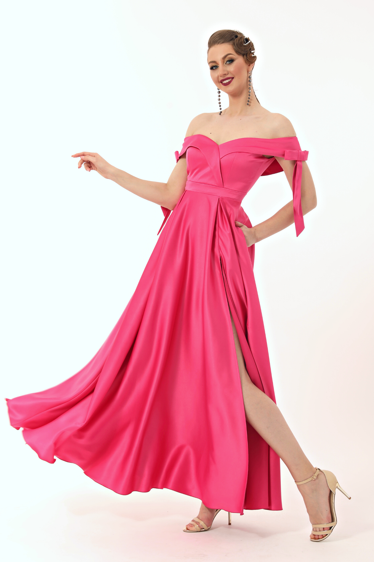 Abito lungo svasato fucsia in taffetà Moda-Mania con scollo a barchetta, spacco laterale e fiocchi decorativi.