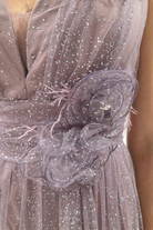Abito lungo svasato lilla in tulle glitterato con spacco e decorazioni floreali, perfetto per occasioni eleganti.