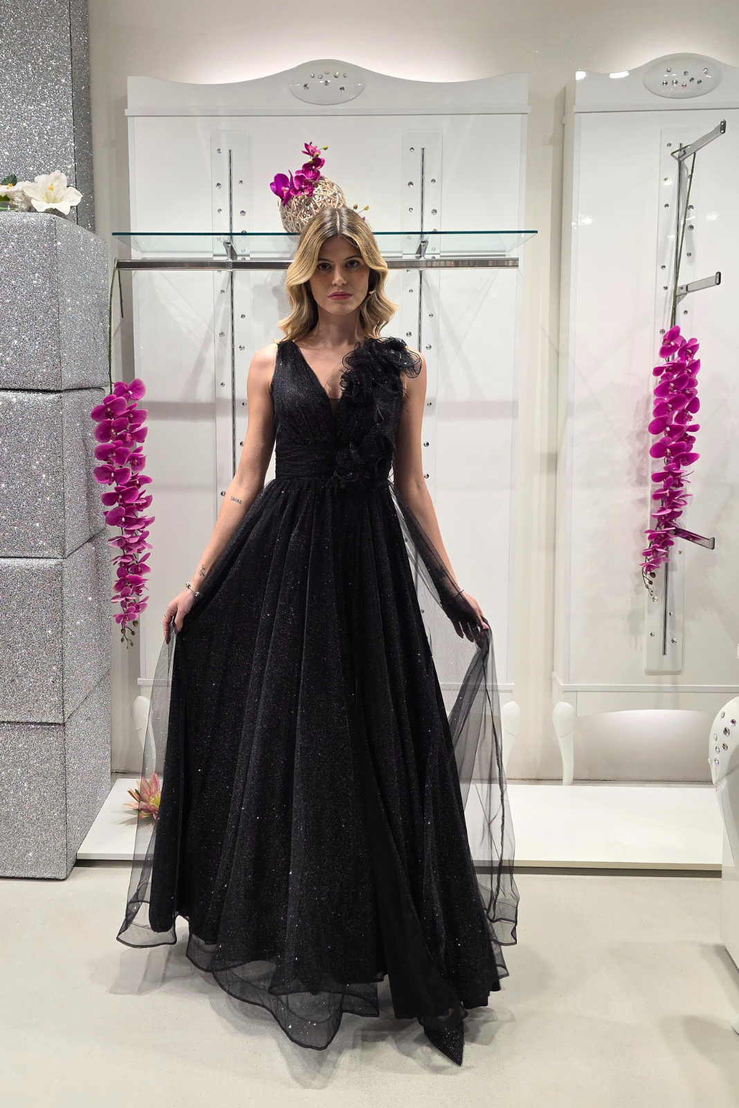 Abito lungo svasato nero in tulle glitterato con spacco e decorazioni floreali, firmato Moda-Mania, visibile in dettaglio.
