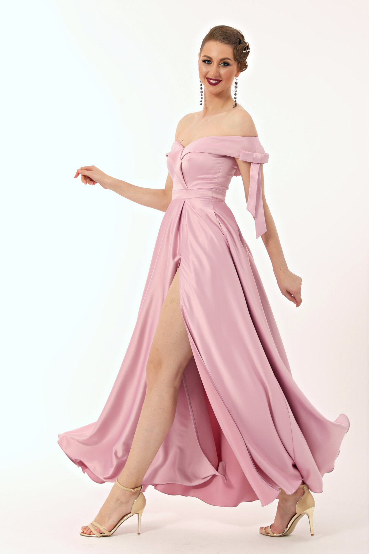 Abito lungo svasato rosa in taffetà di Moda-Mania con scollo a barchetta, spacco laterale e fiocchi decorativi.