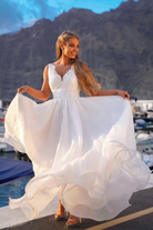 Abito lungo da cerimonia bianco Moda-Mania con corpetto ricamato e gonna ampia in organza su sfondo rosa cipria.
