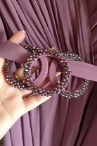 Abito lungo svasato per donne curvy in lavanda viola con maniche a campana, cinturino in vita e accessorio.
