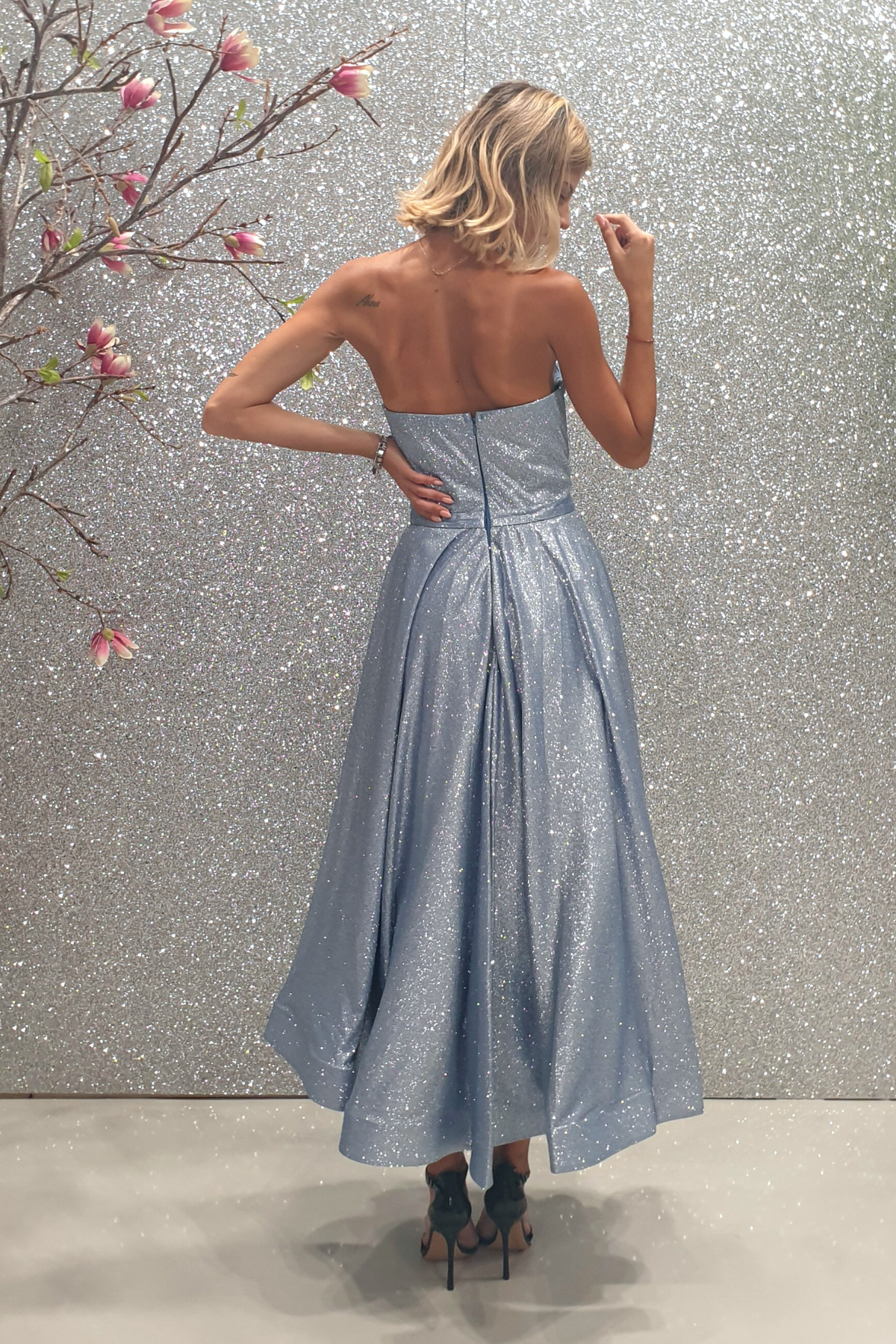Abito lungo svasato in tessuto glitterato celeste, con corpetto a cuore a punta e lunghezza asimmetrica, di Moda-Mania.