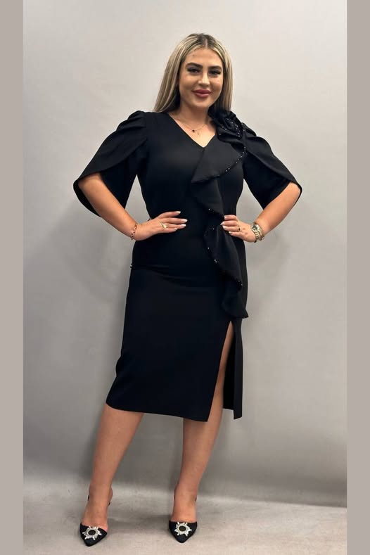 Abito tubino nero aderente per donne curvy di Moda-Mania, con fiore decorativo, volants e spacco, abbigliamento elegante e femminile.