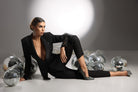 Completo tailleur nero Bby con giacca a revers profondi e applicazioni di paillettes, perline e piume, su sfondo chiaro.