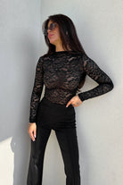 Blusa aderente nera Moda-Mania con maniche lunghe in pizzo elasticizzato fantasia floreale, dettaglio elegante e femminile.