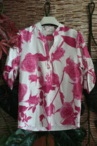 Blusa bianca fantasia floreale fucsia con maniche a tre quarti e bottoni dorati, marca Moda-Mania, vista frontale.
