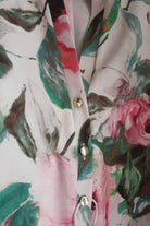 Blusa bianca Moda-Mania con fantasia floreale rosa e foglie, maniche tre quarti e bottoni dorati, dettagli eleganti.