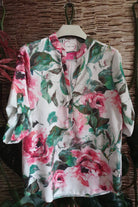 Blusa bianca Moda-Mania con fantasia floreale rosa e foglie, maniche tre quarti e bottoni dorati, dettagli eleganti.