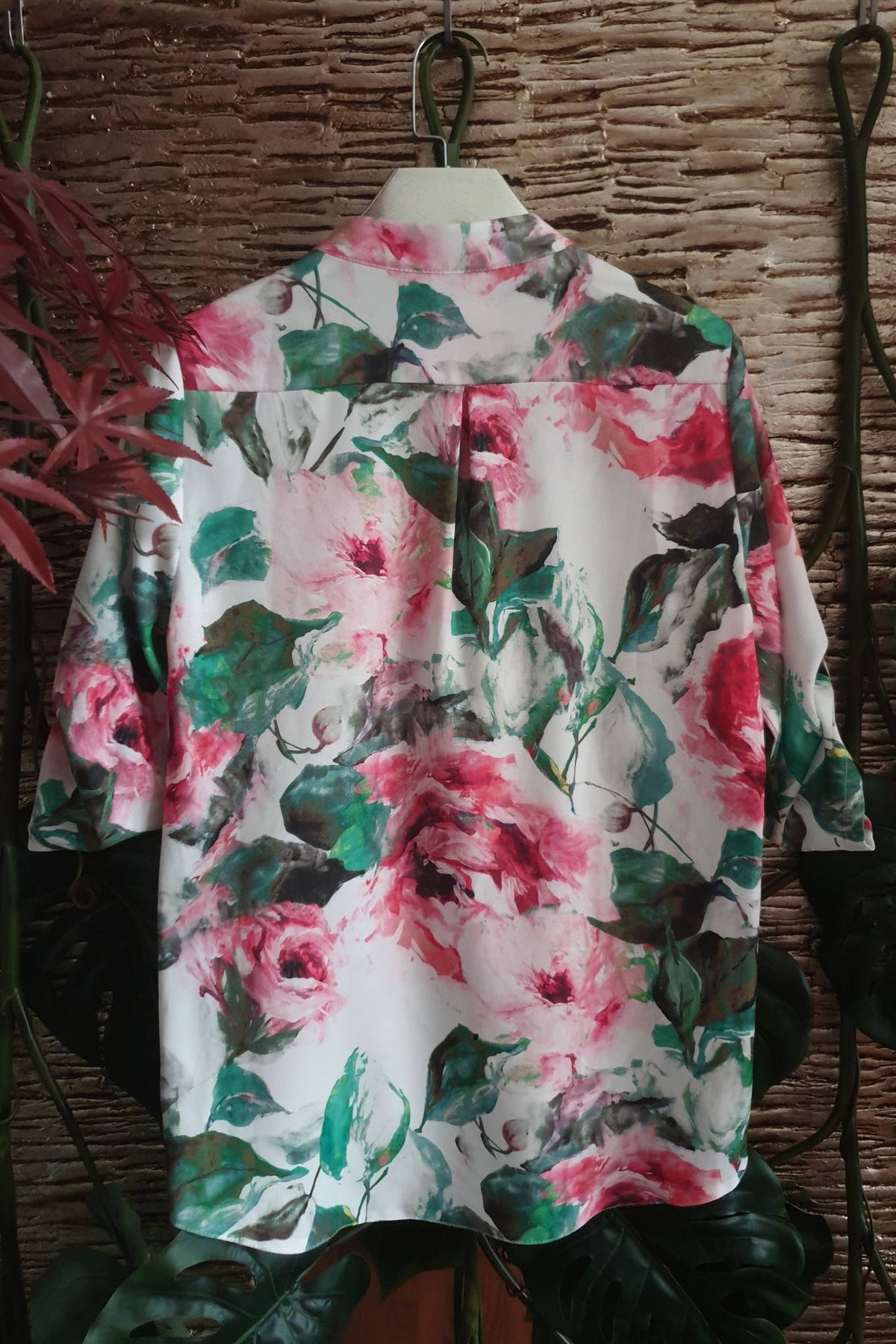 Blusa bianca Moda-Mania con fantasia floreale rosa e foglie, maniche tre quarti e bottoni dorati, visibile in dettaglio.