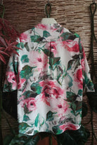 Blusa bianca Moda-Mania con fantasia floreale rosa e foglie, maniche tre quarti e bottoni dorati, visibile in dettaglio.
