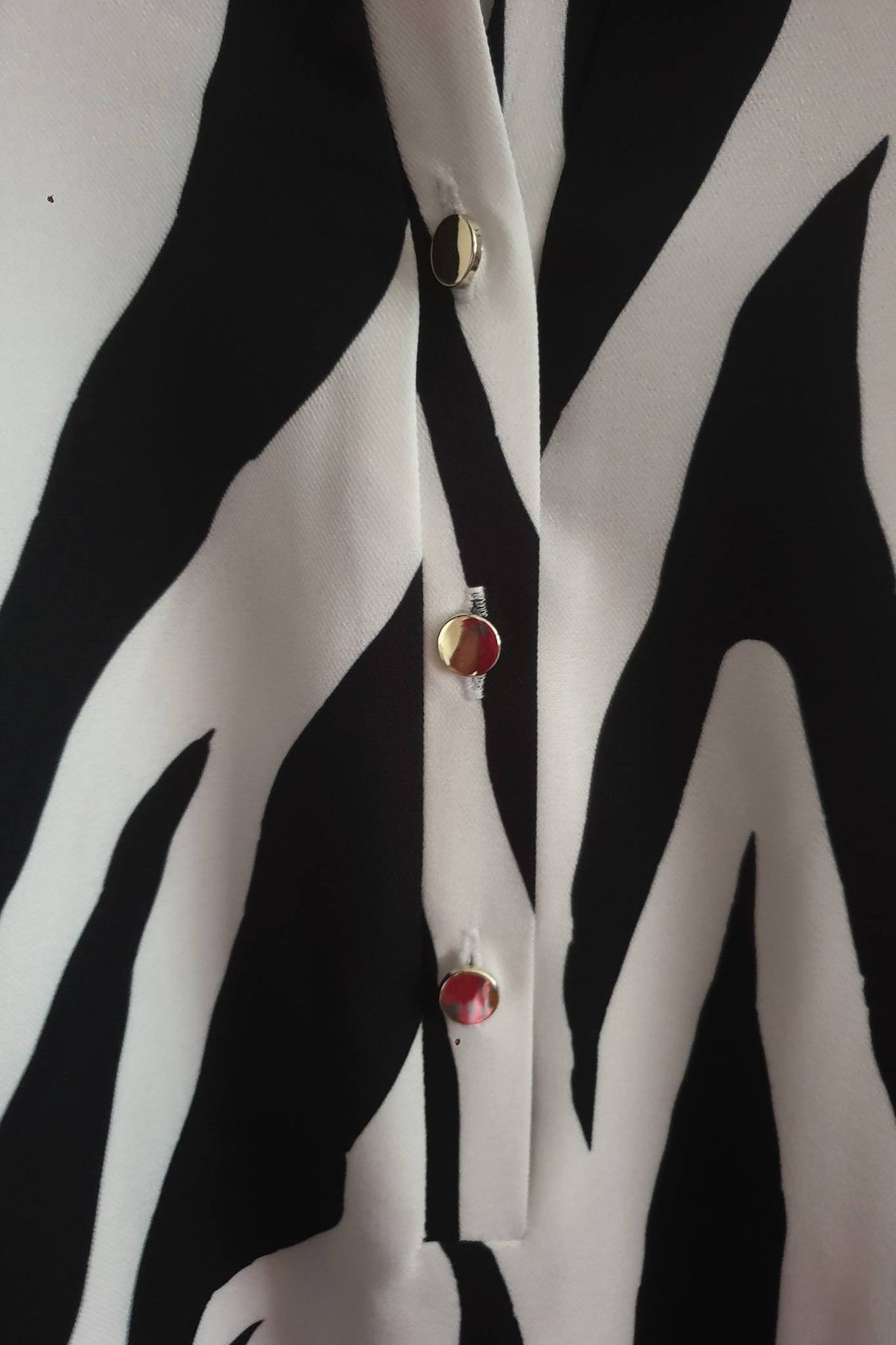 Blusa bianca zebrata Moda-Mania con maniche tre quarti e bottoni dorati, dettaglio di stile e texture animale.