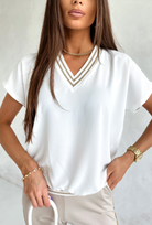 Blusa estiva bianca Moda-Mania con maniche corte e scollo a V dorato, tessuto leggero e dettagli eleganti.