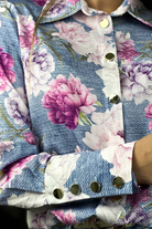 Camicia elegante bianca Moda-Mania con fantasia floreale rosa e bottoni dorati, tessuto leggero e stile raffinato.