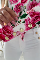 Camicia elegante bianca Moda-Mania con fantasia floreale rosa, dettagli di bottoni dorati, tessuto leggero e stile raffinato.