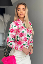 Camicia elegante bianca Moda-Mania con fantasia floreale rosa, bottoni dorati e dettagli raffinati, ideale per look sofisticato.