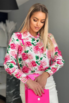 Camicia elegante bianca Moda-Mania con fantasia floreale rosa, bottoni dorati, tessuto leggero e dettagli raffinati.