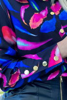 Camicia elegante nera Moda-Mania con fantasia foglie blu e fucsia, bottoni dorati, tessuto leggero e stile raffinato.